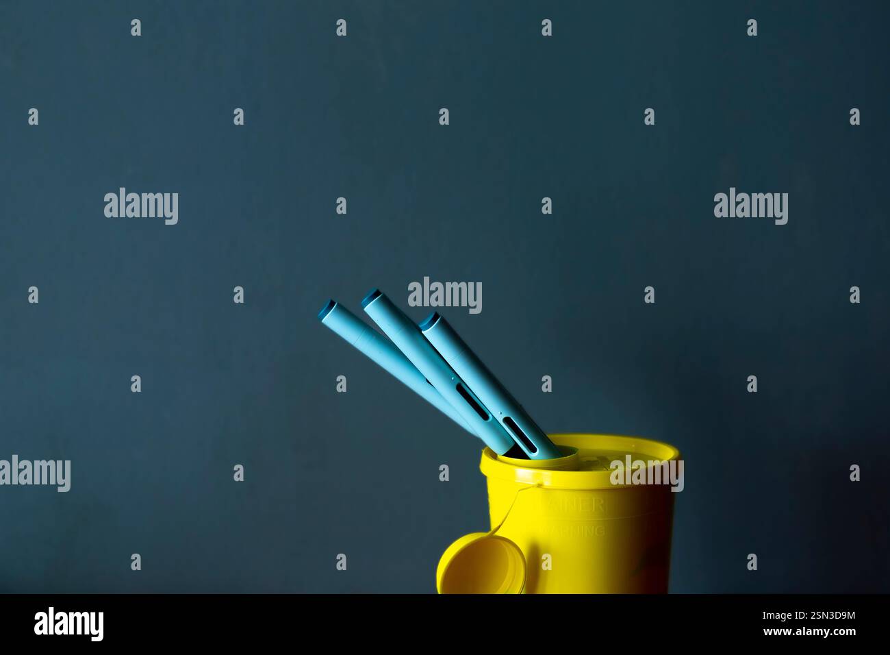 Ein paar Spritzenstifte aus dem Behälter für die Sammelbox für giftigen Abfall, dunkler blaugrüner Hintergrund. Studio Medical Equipment still Life Konzept Stockfoto