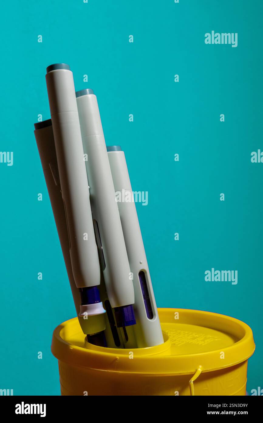 Blaugrüner Rahmen mit Spritzentropfen, die aus dem hellgelben Sammelbehälter für giftigen Abfall ragen. Studio medizinische Geräte Stillleben Konzept mit Auto- Stockfoto