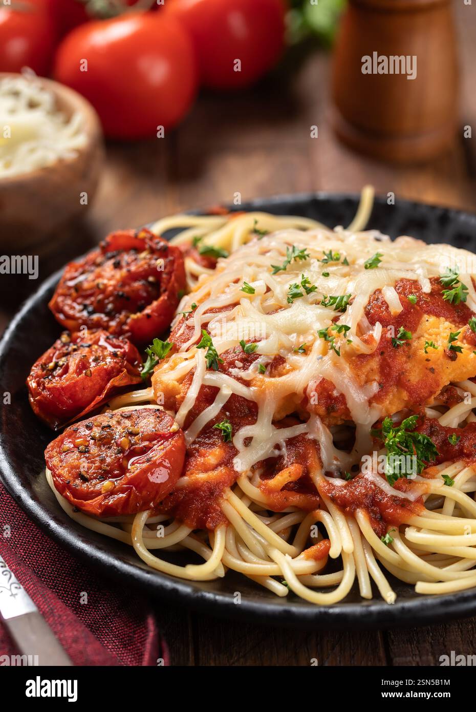 Hühnerparmesan mit Spaghettinudeln, Sauce und gebratenen Tomaten, garniert mit Basilikumblättern und gehackter Petersilie auf einem Teller Stockfoto