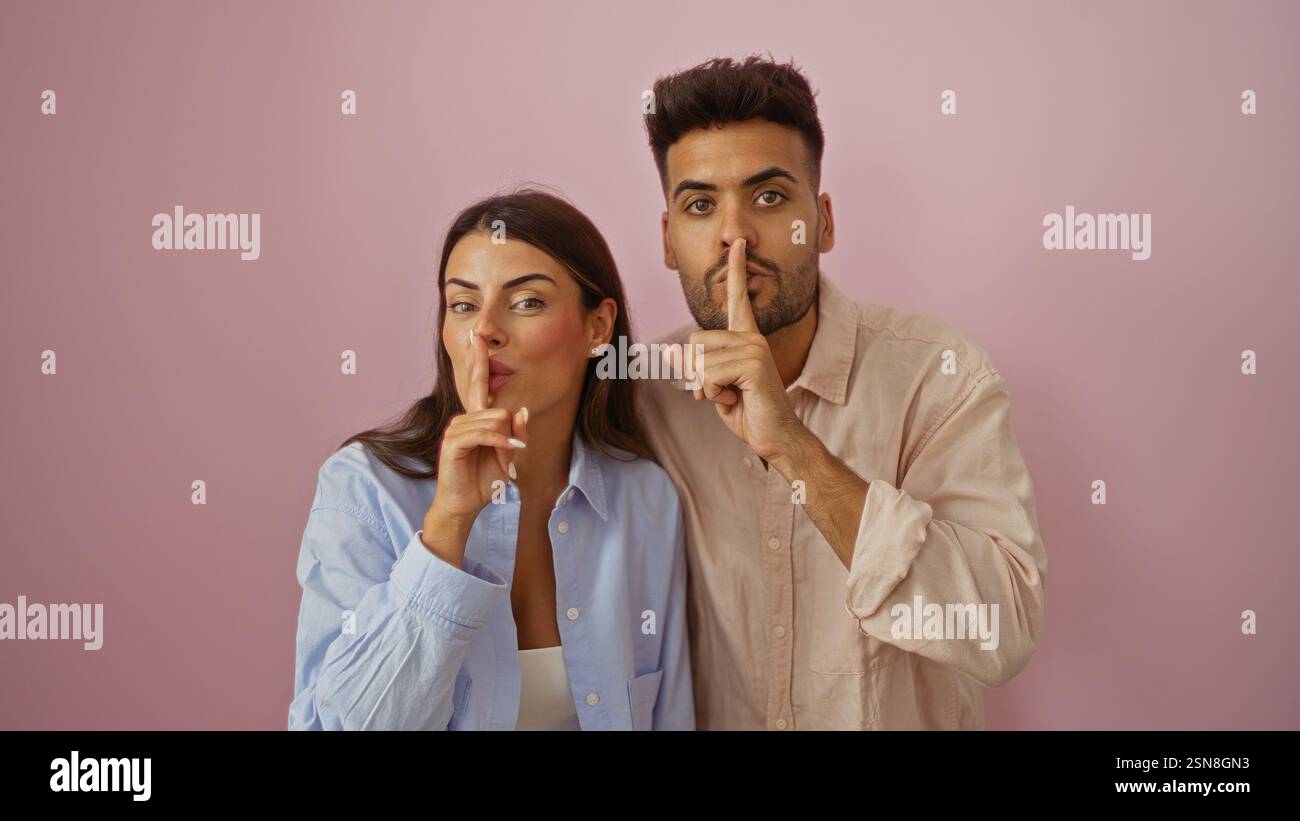 Man kann mit den Fingern auf den Lippen eine Geste machen, während man vor einem rosafarbenen Hintergrund steht und Geheimhaltung oder Ruhe ausdrückt Stockfoto