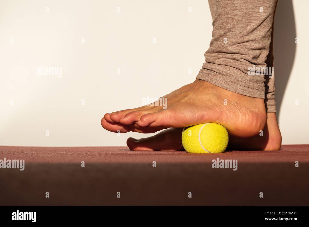 Myofasziale Entspannung der Fussmuskeln mit einem Tennisball auf einer Matte zu Hause, Nahaufnahme. Konzept zum Thema Fussschmerz-Prophylaxe Stockfoto