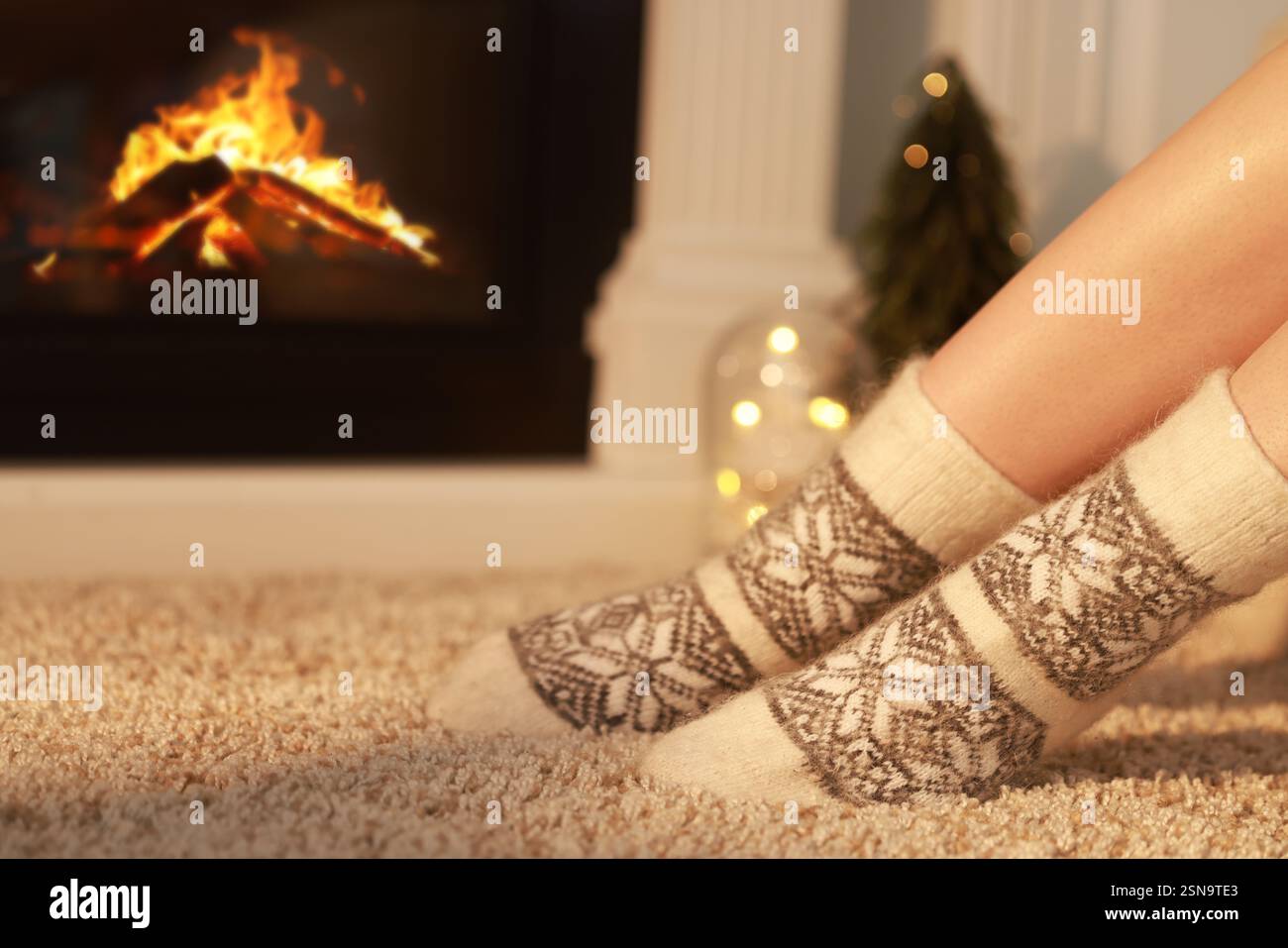 Frau in warmen Socken, die zu Hause am Kamin liegt, Nahaufnahme. Leerzeichen für Text Stockfoto