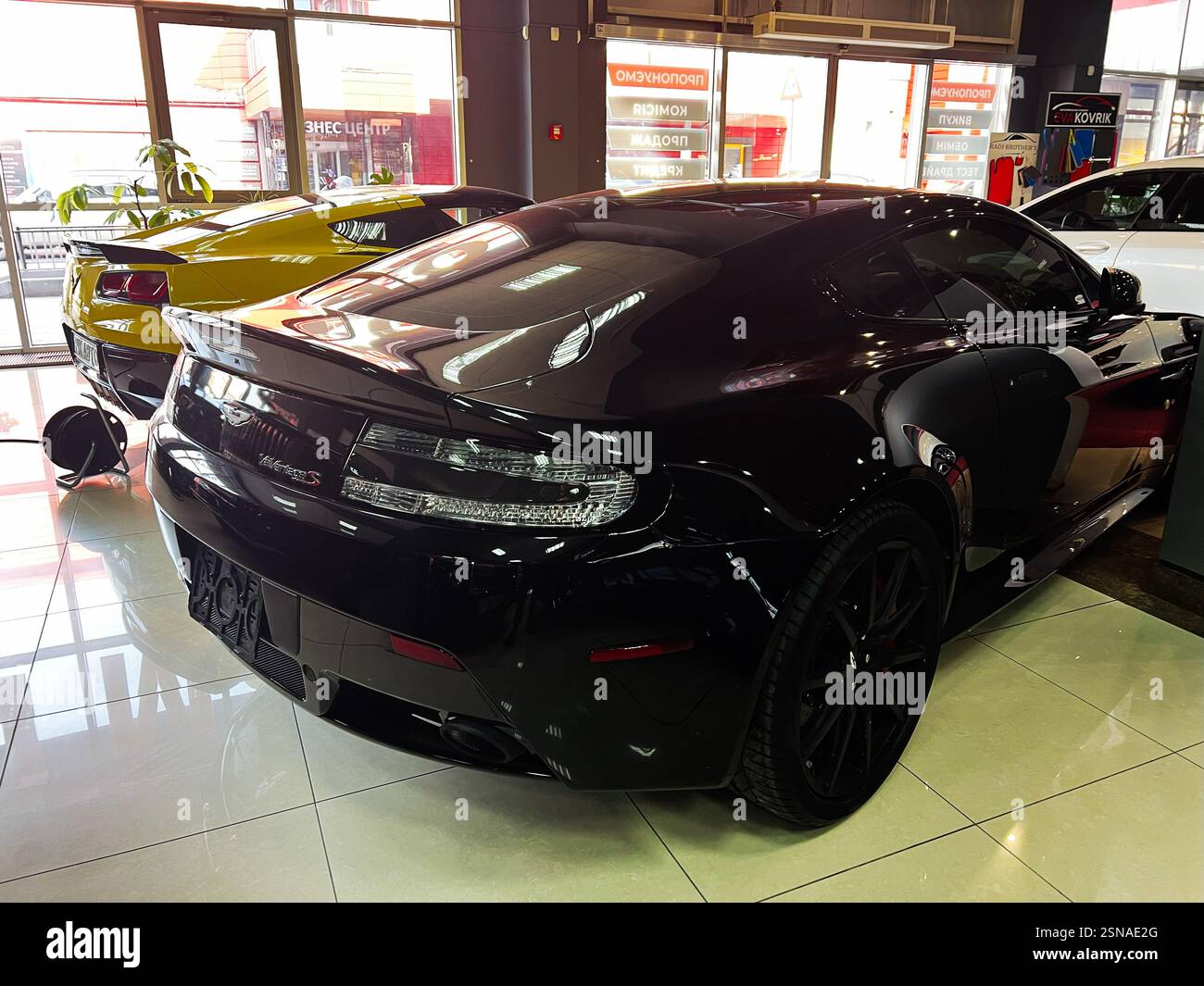 Lviv, Ukraine - 12. Februar 2025: Der glänzend schwarze Sportwagen Aston Martin Vantage S parkt im Innenbereich unter hellen Lichtern mit moderner Architektur. Stockfoto