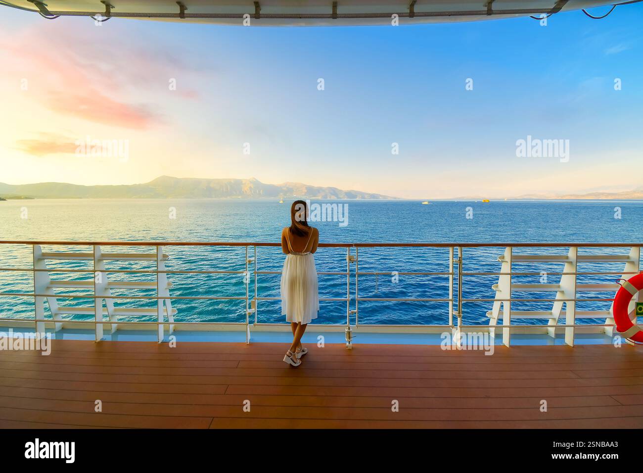 Eine Frau steht bei Sonnenuntergang auf Deck eines Kreuzfahrtschiffs, während es das Mittelmeer durchquert und an griechischen Inseln in der Nähe von Korfu Griechenland vorbeifährt. Stockfoto
