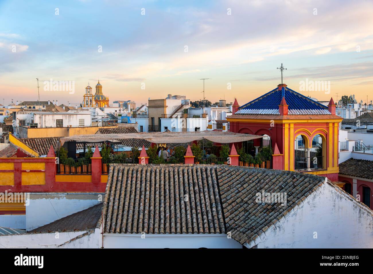 Eine Party bei Sonnenuntergang in einem Dachgarten im Viertel Barrio Santa Cruz in Sevilla, Spanien, mit der Kuppel und den Glocken von Iglesia de Santa Cruz dahinter. Stockfoto