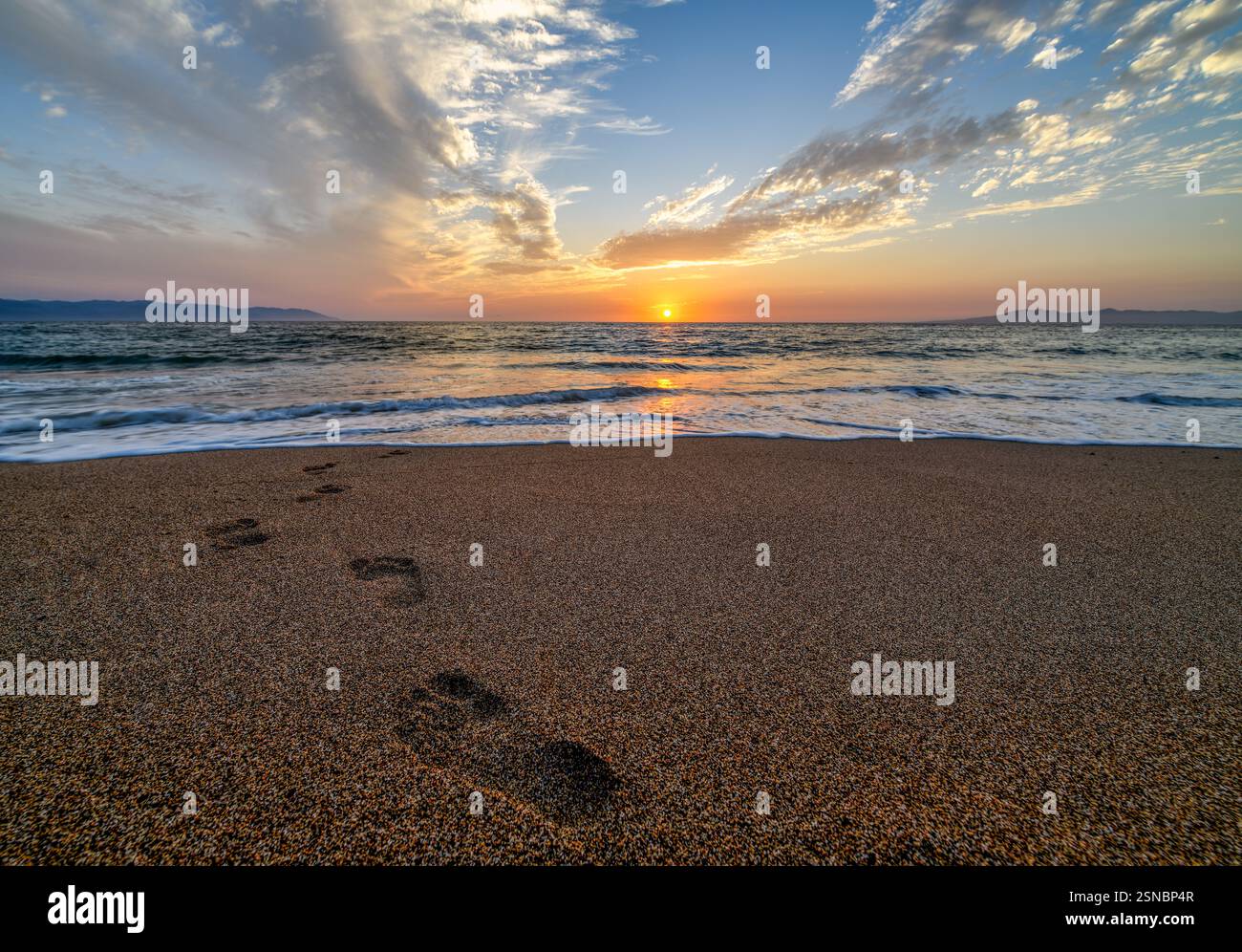 Fußspuren im Sand, die zum Sonnenaufgang des Ozeans führen Stockfoto