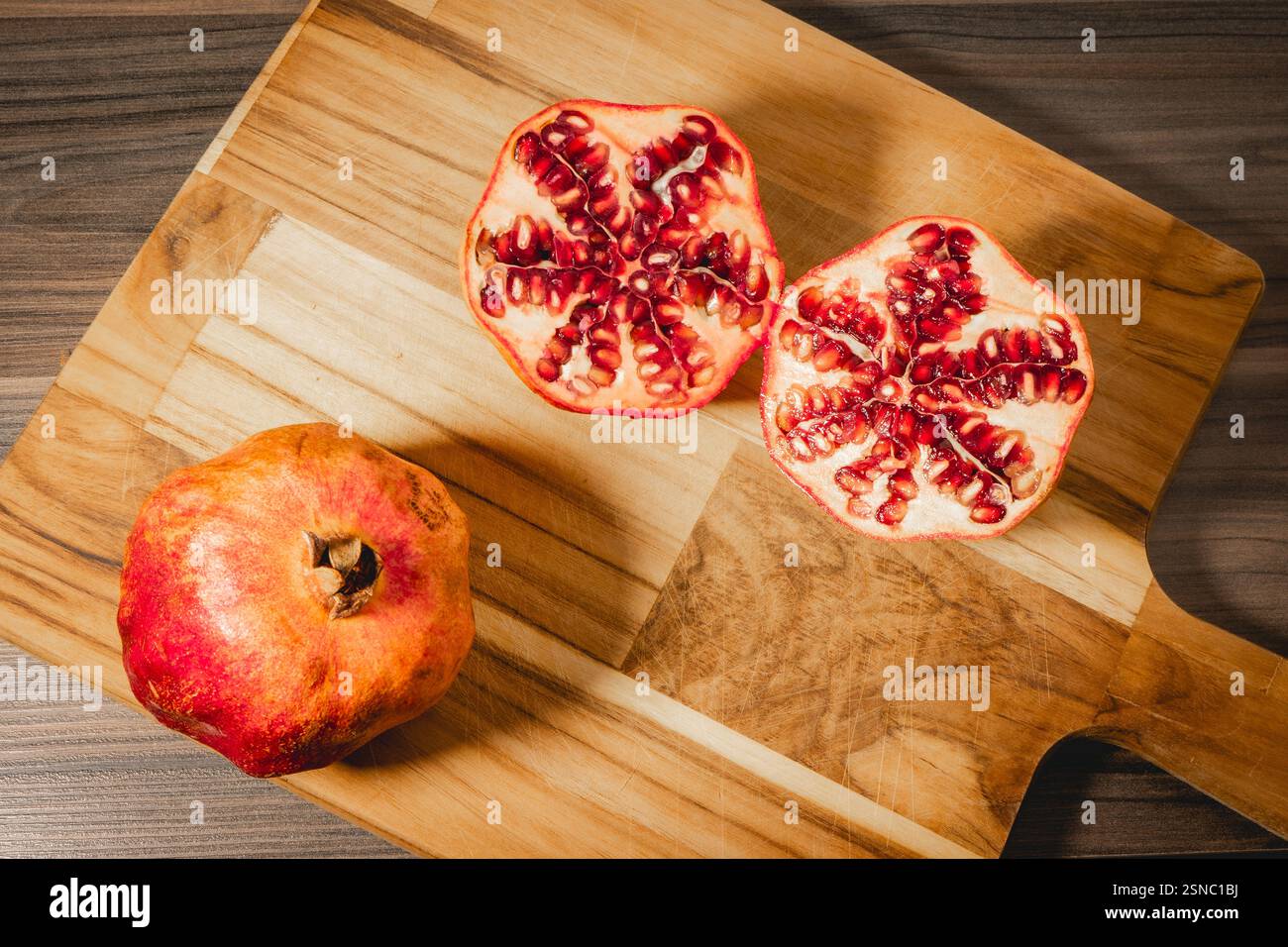 Pomegranaten in zwei Hälften auf hölzernem Hintergrund. Stockfoto