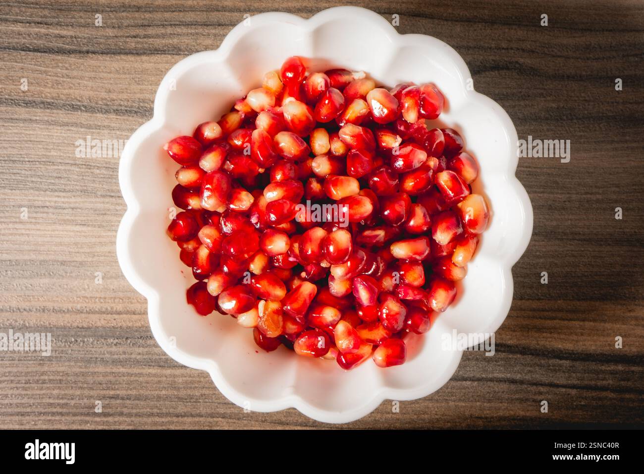 Eine weiße Schüssel mit Samen von Pomegrenade, auf einem hölzernen Hintergrund. Stockfoto