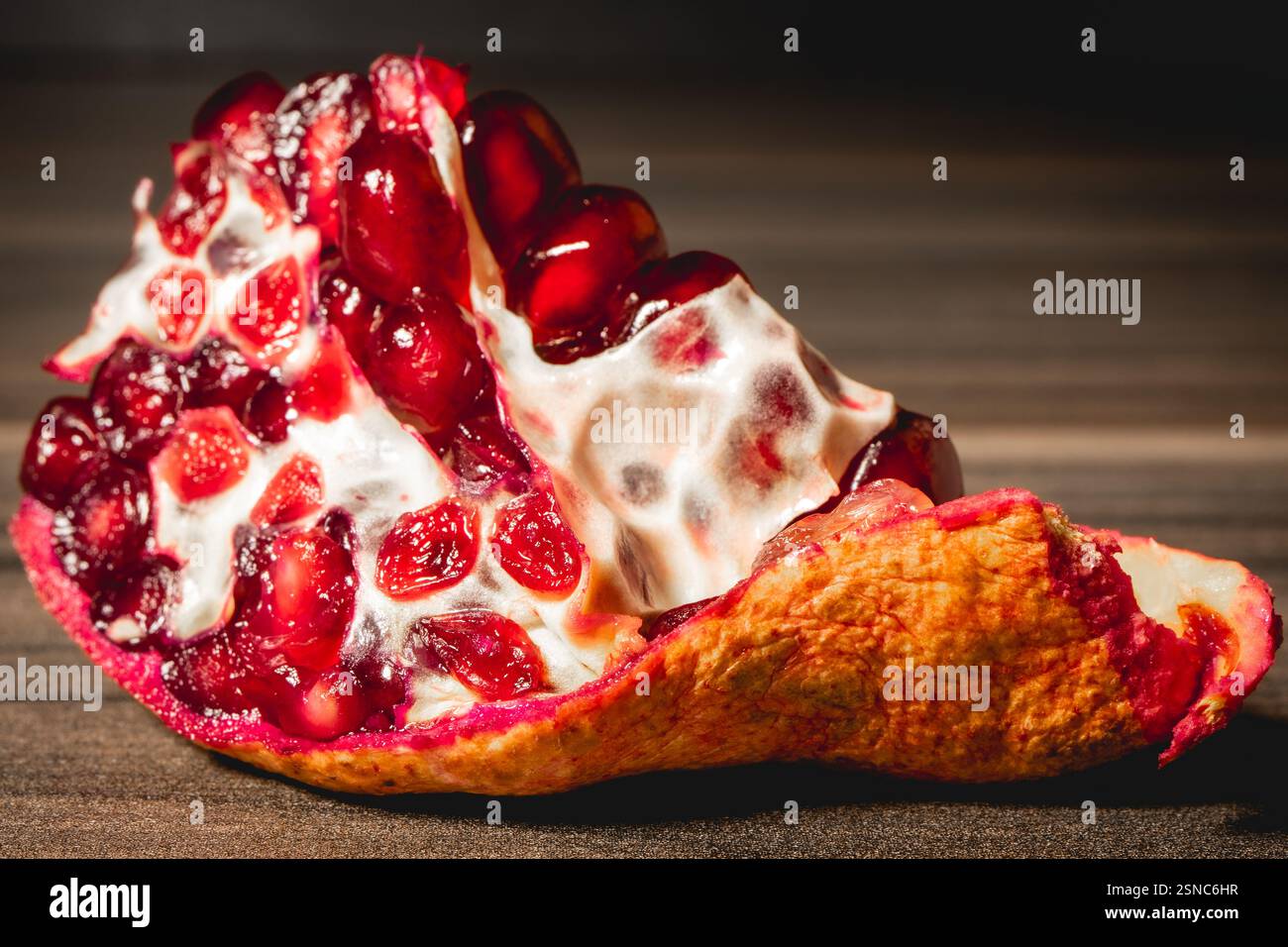 O Frieden einer Pomegranade mit den Samen im Inneren, auf einem hölzernen Hintergrund. Stockfoto