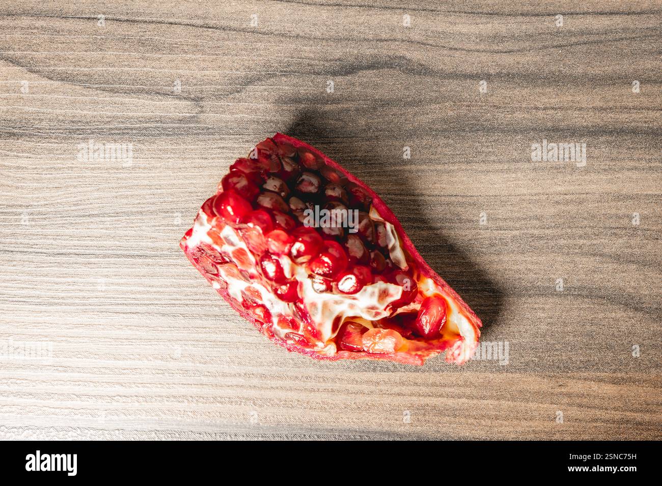 O Frieden einer Pomegranade mit den Samen im Inneren, auf einem hölzernen Hintergrund. Stockfoto