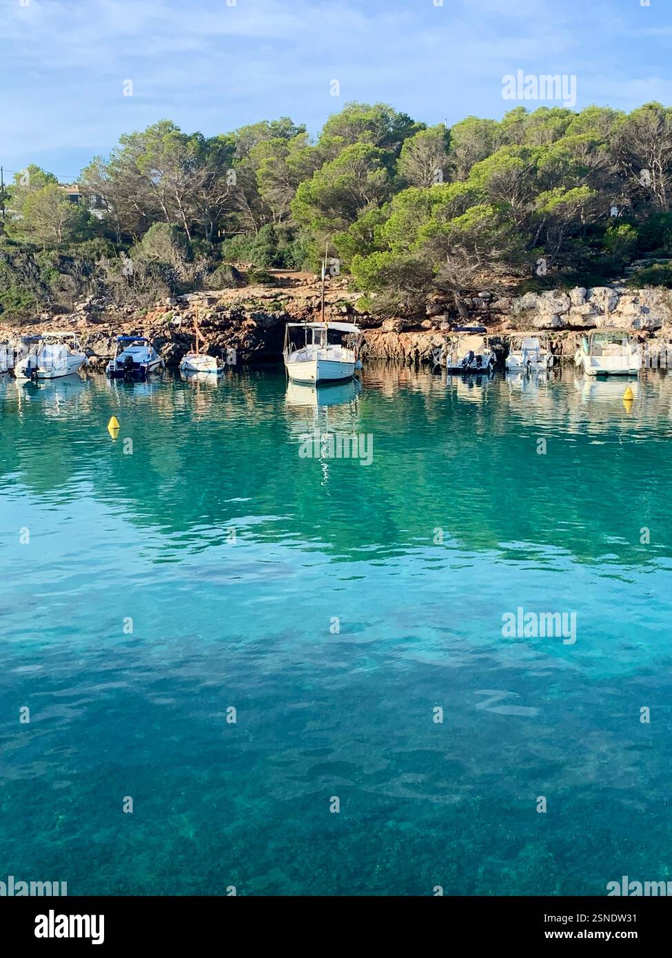 Boote liegen neben dem felsigen Ufer auf dem türkisfarbenen Meer auf Menorca - Smartphone-aufgenommenes Stockfoto