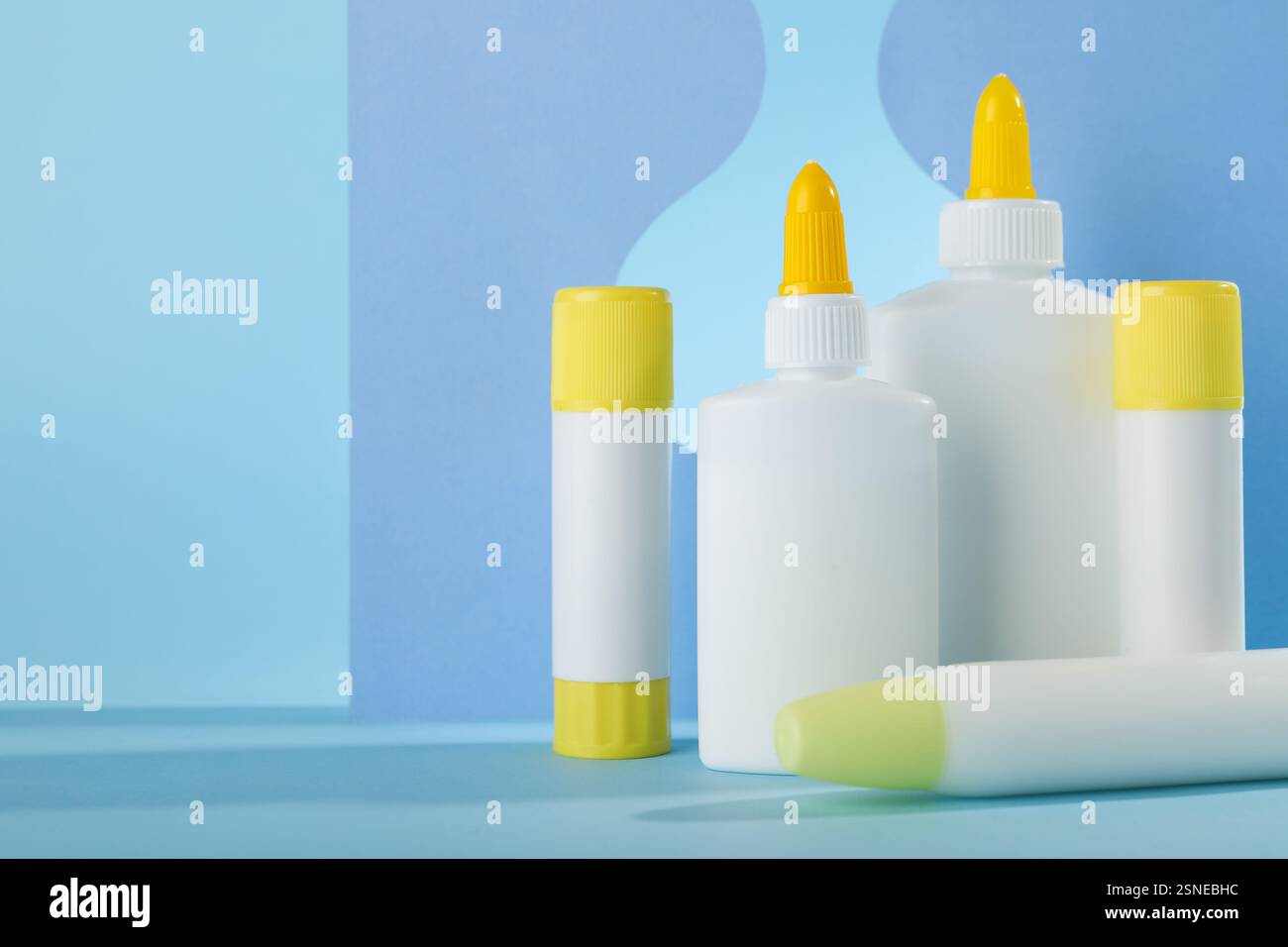 Verschiedene Arten von Klebstoff und Papierausschnitten auf hellblauem Hintergrund, Platz für Text Stockfoto