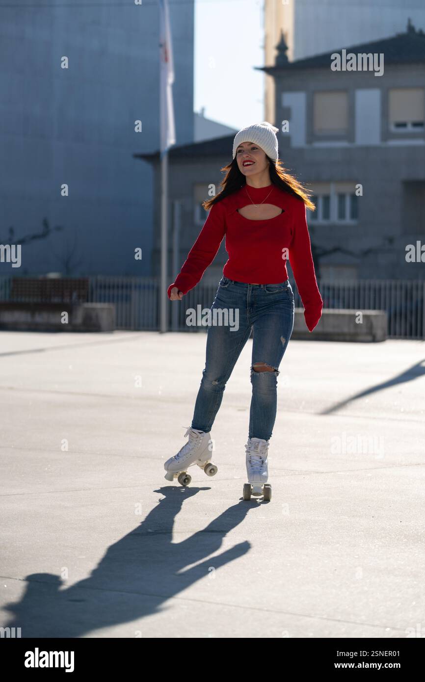 Junge Frau mit einem leuchtend roten Pullover und einer gemütlichen weißen Mütze, die durch eine urbane Landschaft fährt und einen aktiven und gesunden Lebensstil feiert Stockfoto