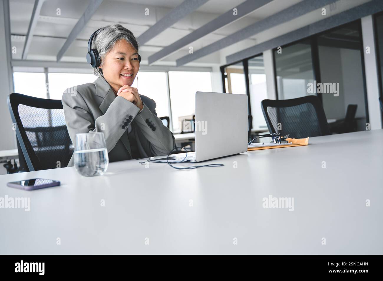 Beschäftigte, reife asiatische Geschäftsfrau, die im Büro an einem Laptop arbeitet und das Webinar ansieht. Stockfoto