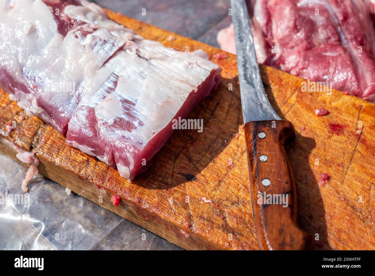 Schneidebrett mit rohem Schweinefleisch und Küchenmesser auf einem Holztisch. Selektiver Fokus. Stockfoto