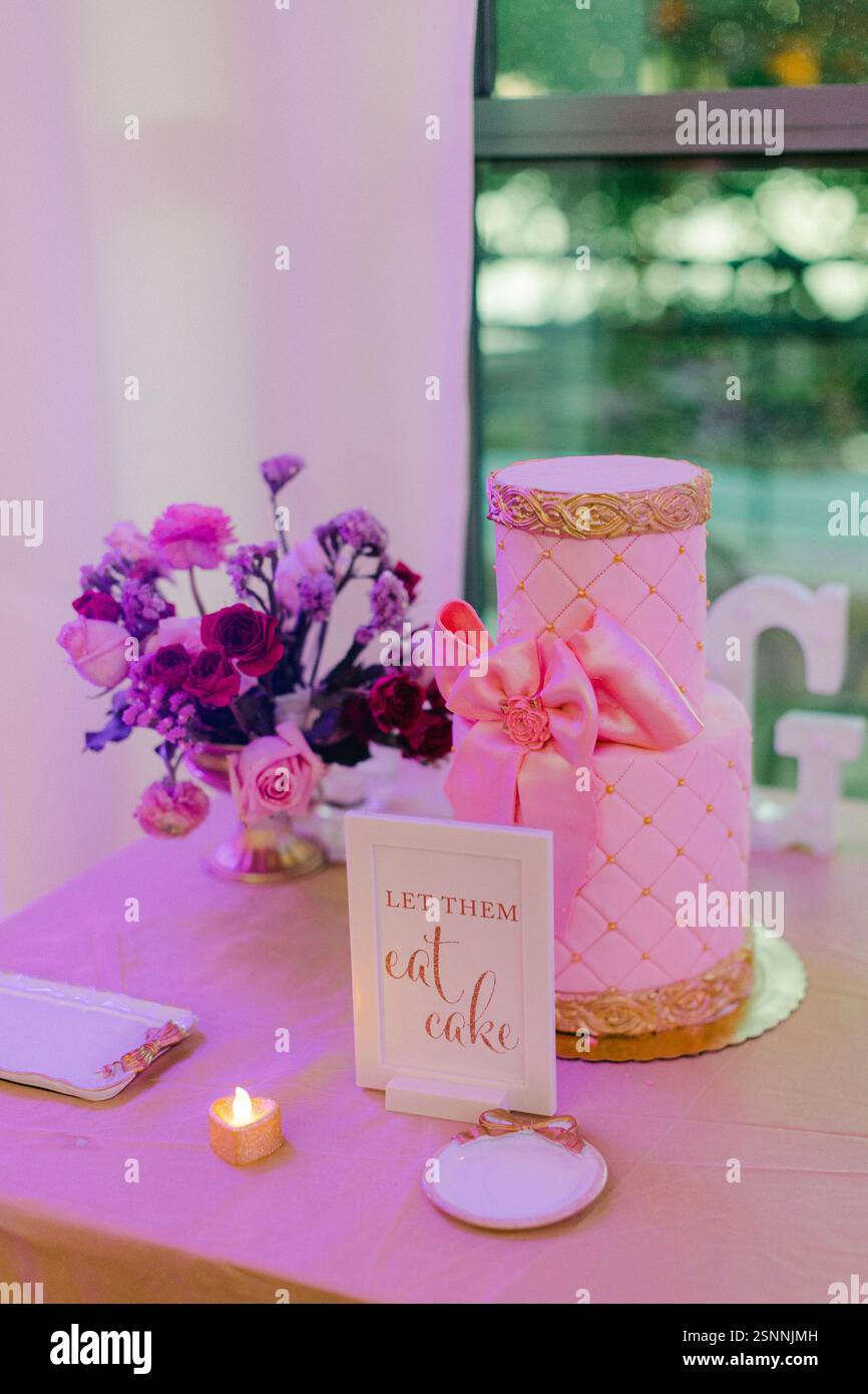 Ein lebhafter Tisch mit rosa Kuchen, frischen Blumen und einem verspielten Schild feiert freudige Momente. Stockfoto