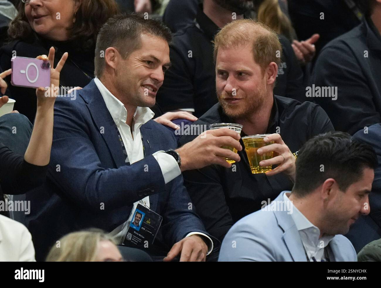 British Prince Harry, right, the Duke of Sussex, drinks beer with retired New Zealand rugby player Richie McCaw while watching the U.S. and Australia play the bronze medal wheelchair rugby match during the 2025 Invictus Games, in Vancouver, on Thursday, Feb. 13, 2025. (Darryl Dyck/The Canadian Press via AP) Stockfoto