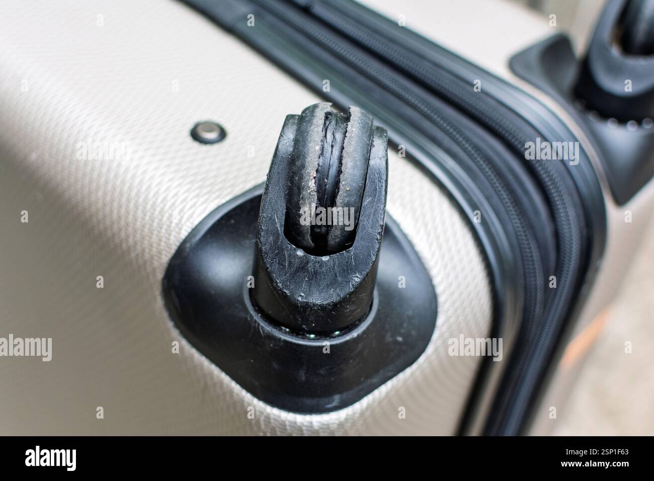 Beschädigtes Gepäckrad an einem strukturierten beigefarbenen Koffer mit sichtbaren Reißverschlüssen und Kunststoffgehäuse. Nahaufnahme. Stockfoto