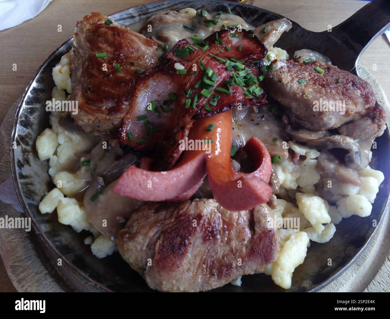 Herzhafte Platte mit gegrilltem Fleisch, Würstchen und Knödeln, getränkt mit reichhaltiger Soße. Eine herzhafte und erfüllende Mahlzeit, die perfekt ist, um Heißhunger zu stillen. Germa Stockfoto
