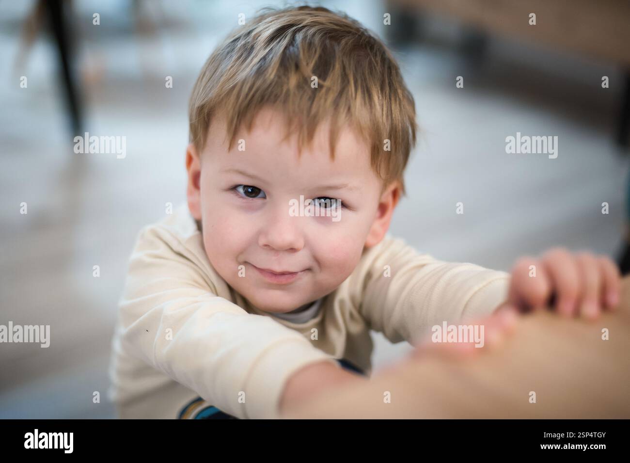 Ein kleines Kind mit hellbraunem Haar lächelt und streckt neugierig in einer warmen, einladenden Innenumgebung aus, um die Unschuld des Kindes zu zeigen Stockfoto