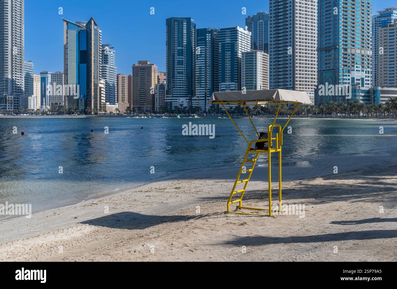 Unbewohnt, gelb, Rettungswache am Strand von Sharjah, nördlich von Dubai. Im Hintergrund befindet sich die beliebte Stadtlandschaft am Wasser. Stockfoto