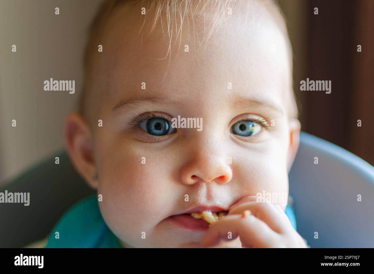 Nahaufnahme eines blauäugigen Babys im Lätzchen, das ihr Essen in den Mund steckt Stockfoto