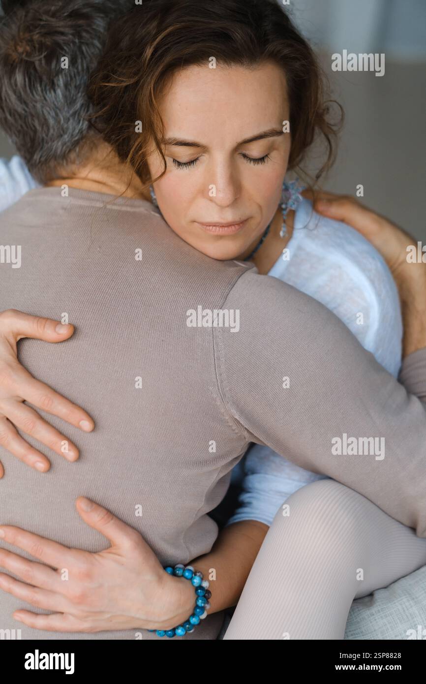 Ein Paar sitzt auf einer weichen Matte in einem luftigen Studio, umgeben von einer warmen Umarmung, Augen geschlossen, genießen einen friedlichen Moment der Verbindung und Meditation Stockfoto