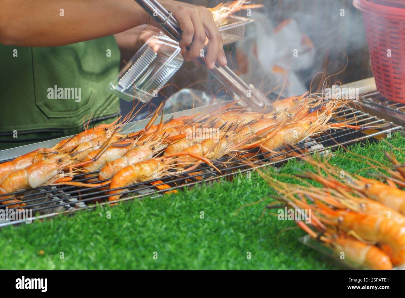 Nahaufnahme von frischen Flussgarnelen, die über einer heißen Flamme in einem belebten Street Food Stand gegrillt werden. Ihre leuchtenden Orangenschalen und das rauchige Aroma fangen ein Stockfoto