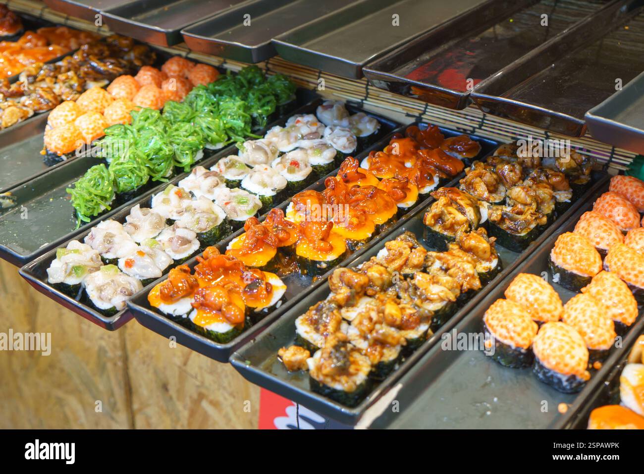 Nahaufnahme verschiedener Sushi-Sorten, die an einem Street Food-Stand gezeigt werden, mit Algensalat, Oktopus, Muscheln, Lachsrogen, und gegrillter Aal. Stockfoto