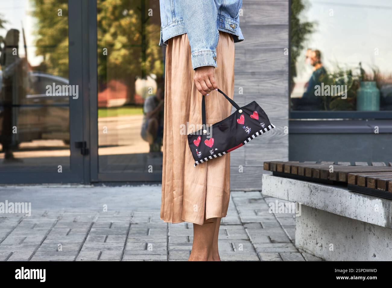 Stilvoll hält die Frau eine dekorative Geldbörse mit farbenfrohen Herzen in Jeansjacke und -Rock, Urban Street Concept Stockfoto