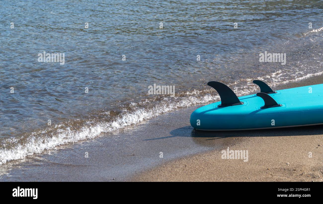 Ein Stand-up-Paddleboard liegt an der Küste, während sanfte Meereswellen über sie strömen und eine ruhige und einladende Wassersportszene am Sarsala Beach, Dala, schaffen Stockfoto