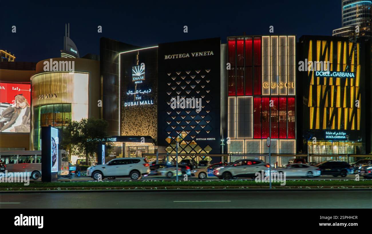Dubai, VAE - 13. November 2024: Der geschäftige Stadtverkehr fließt bei Nacht an der beleuchteten Dubai Mall vorbei, mit streifendem Autolampen und urbaner Energie, die das VI prägen Stockfoto