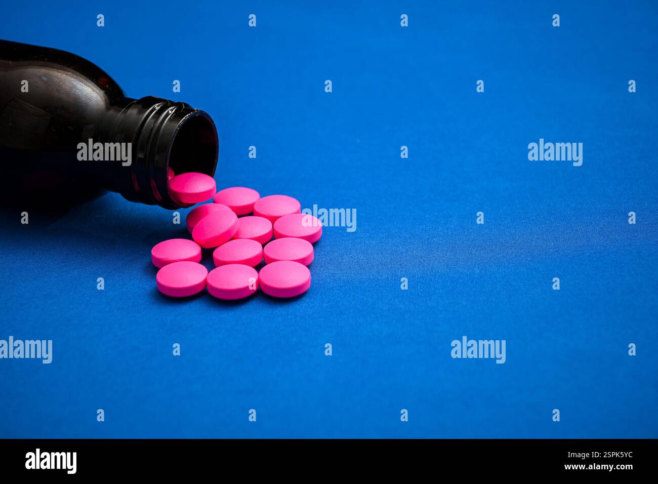 Pinkfarbene Pillen aus einer dunklen Arzneiflasche auf blauem Hintergrund erzeugen einen auffälligen Kontrast. Stockfoto