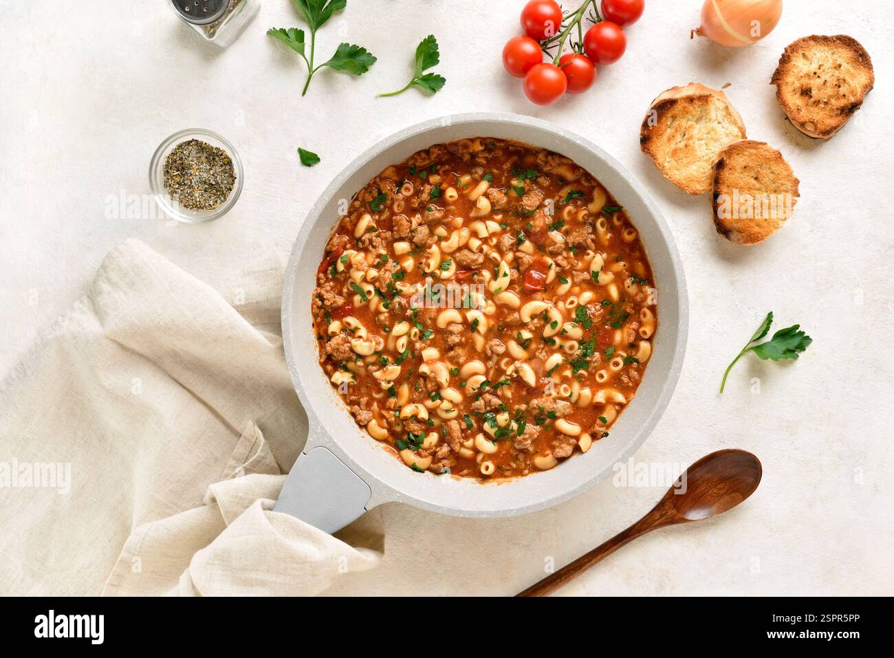 Eine Topfmahlzeit mit Hackfleisch, Pasta und Gemüse in Tomatensoße in einer Pfanne auf hellem Steinhintergrund gekocht. Draufsicht, flach Stockfoto
