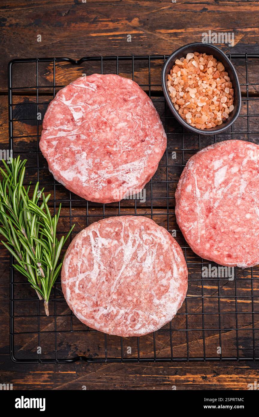 Gefrorene Fleischpasteten, bereit zum Grillen, Forcemeat von Schwein und Rindfleisch für Burger. Hölzerner Hintergrund. Draufsicht Stockfoto