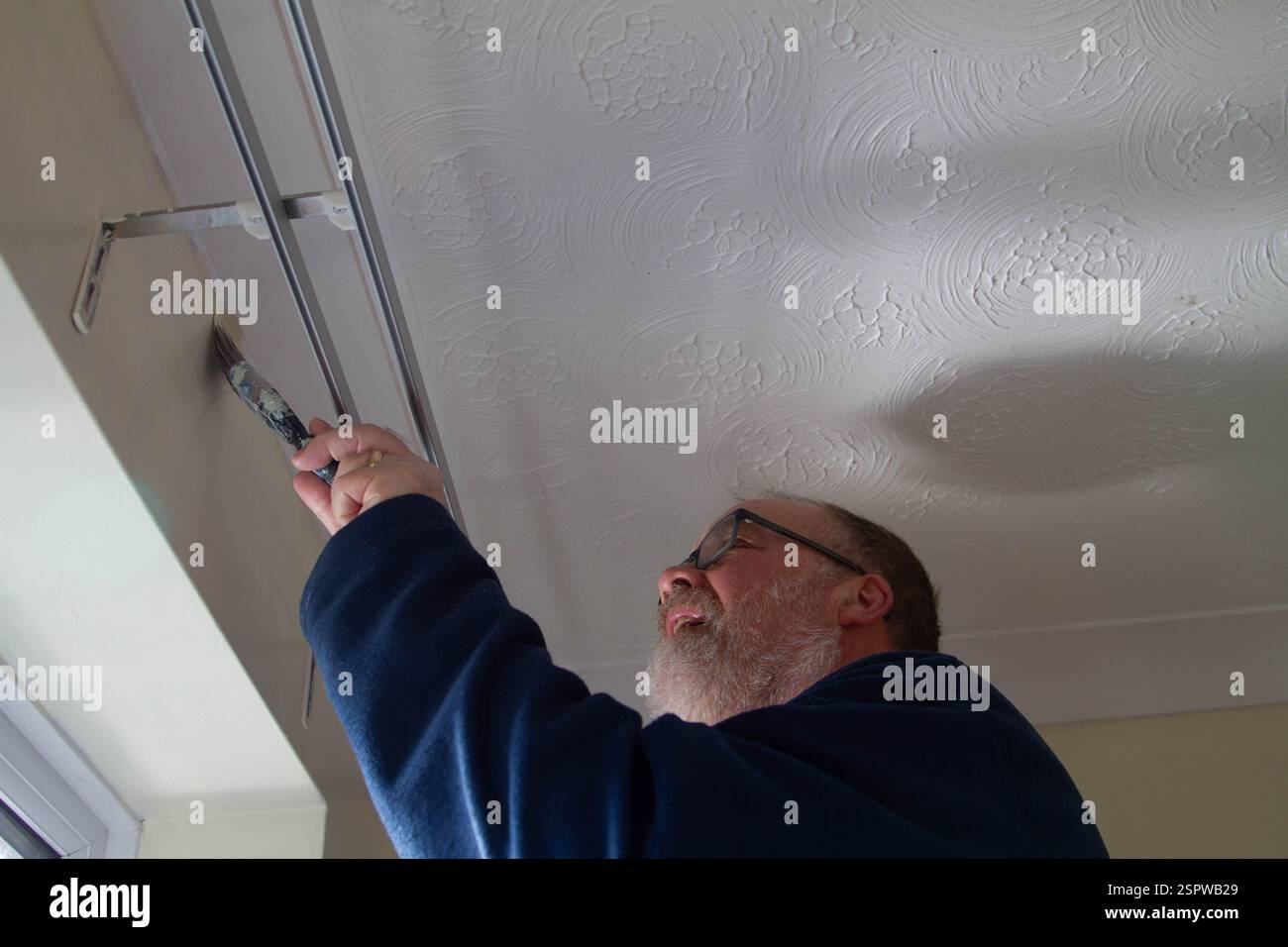 Mann mittleren Alters, der um ein Fenster malt Stockfoto