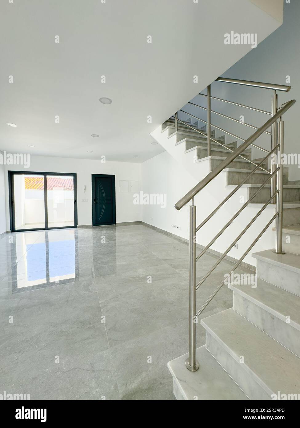 Moderner, offener Wohnbereich mit Edelstahltreppe und reflektierendem Fliesenboden. Stockfoto