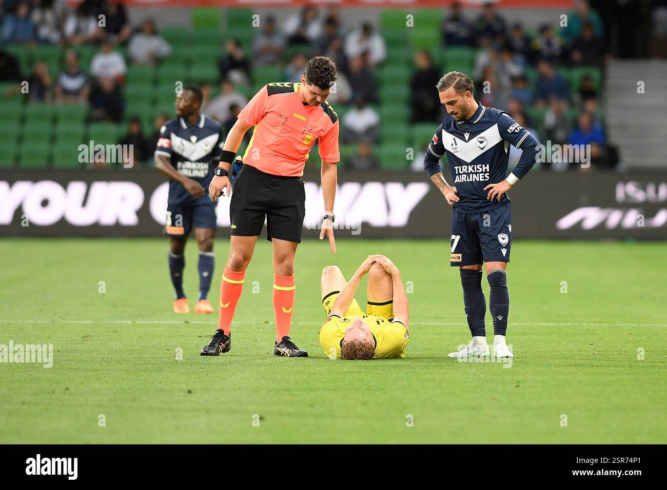 MELBOURNE, AUSTRALIEN. Februar 2025. Im Bild: Match-Schiedsrichter Adam Bavcar (links) spricht mit einem verletzten Wellington Phoenix-Verteidiger Corban Piper, der sein rechtes Knie unter dem wachsamen Auge von Reno Piscopo von Melbourne Victory (rechts) während des Spiels der ISUZU A League Runde 19, Melbourne Victory gegen Wellington Phoenix im AAMI Park, Melbourne, Australien am 14. Februar 2025 festhält. Quelle: Karl Phillipson / Alamy Live News Stockfoto