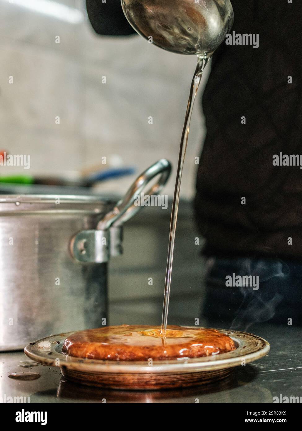 Sherbet wird über die Kunafa gegossen. Kunafa, das berühmte Dessert des Nahen Ostens, ist der unentbehrlichste und klarste Geschmack der arabischen Küche. Das Zentrum von Kunafa ist Antakya, eine ehemalige syrische Provinz. Von der osmanischen Zeit bis heute hat Antakya Kunafa seinen Ruf berühmt gemacht. Antakya Kunafa ist eines der wenigen in der Türkei hergestellten Desserts mit Käse. In der Herstellung von Kadayif werden frischer Kunafa-Käse, Butter und Sherbet verwendet. Er wird durch das Kochen von Kunafa-Käse zwischen zwei Lagen Drahtsammelkadayif in einem flachen Tablett und Zugabe von Sherbet zu der gewünschten Süßigkeit gewonnen Stockfoto