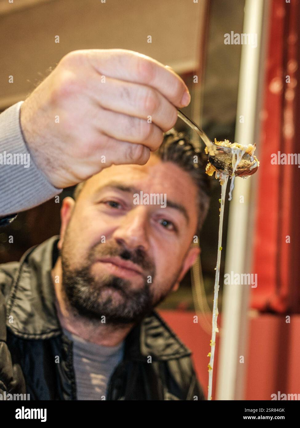 Ein Mann isst eine Kunafa. Kunafa, das berühmte Dessert des Nahen Ostens, ist der unentbehrlichste und klarste Geschmack der arabischen Küche. Das Zentrum von Kunafa ist Antakya, eine ehemalige syrische Provinz. Von der osmanischen Zeit bis heute hat Antakya Kunafa seinen Ruf berühmt gemacht. Antakya Kunafa ist eines der wenigen in der Türkei hergestellten Desserts mit Käse. In der Herstellung von Kadayif werden frischer Kunafa-Käse, Butter und Sherbet verwendet. Er wird durch das Kochen von Kunafa-Käse zwischen zwei Lagen Drahtsammelkadayif in einem flachen Tablett und Zugabe von Sherbet zur gewünschten Süße gewonnen. Die Si Stockfoto
