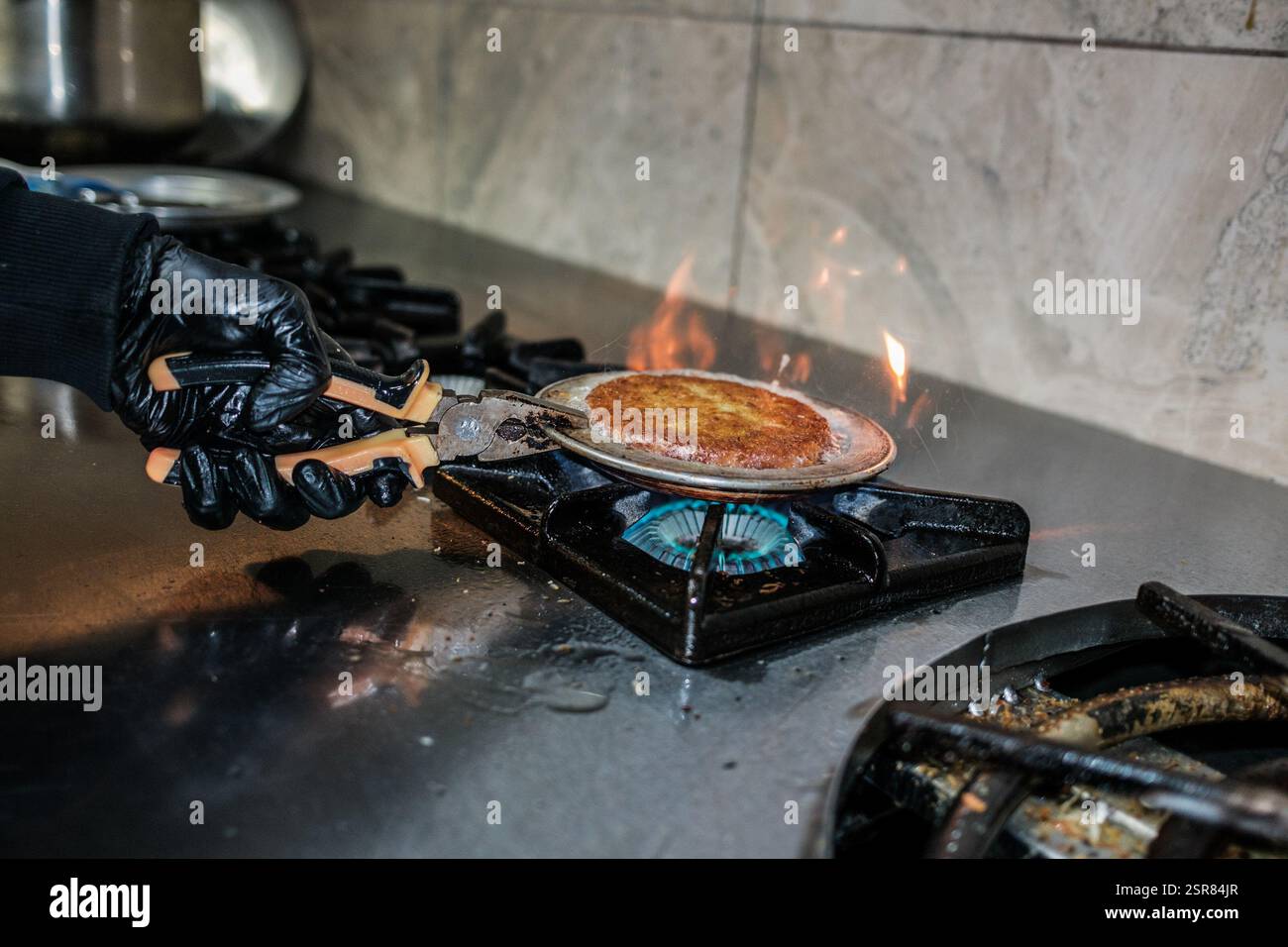 Ein Koch kocht Kunafa. Kunafa, das berühmte Dessert des Nahen Ostens, ist der unentbehrlichste und klarste Geschmack der arabischen Küche. Das Zentrum von Kunafa ist Antakya, eine ehemalige syrische Provinz. Von der osmanischen Zeit bis heute hat Antakya Kunafa seinen Ruf berühmt gemacht. Antakya Kunafa ist eines der wenigen in der Türkei hergestellten Desserts mit Käse. In der Herstellung von Kadayif werden frischer Kunafa-Käse, Butter und Sherbet verwendet. Er wird durch das Kochen von Kunafa-Käse zwischen zwei Lagen Drahtsammelkadayif in einem flachen Tablett und Zugabe von Sherbet zur gewünschten Süße gewonnen. Die Größe Stockfoto