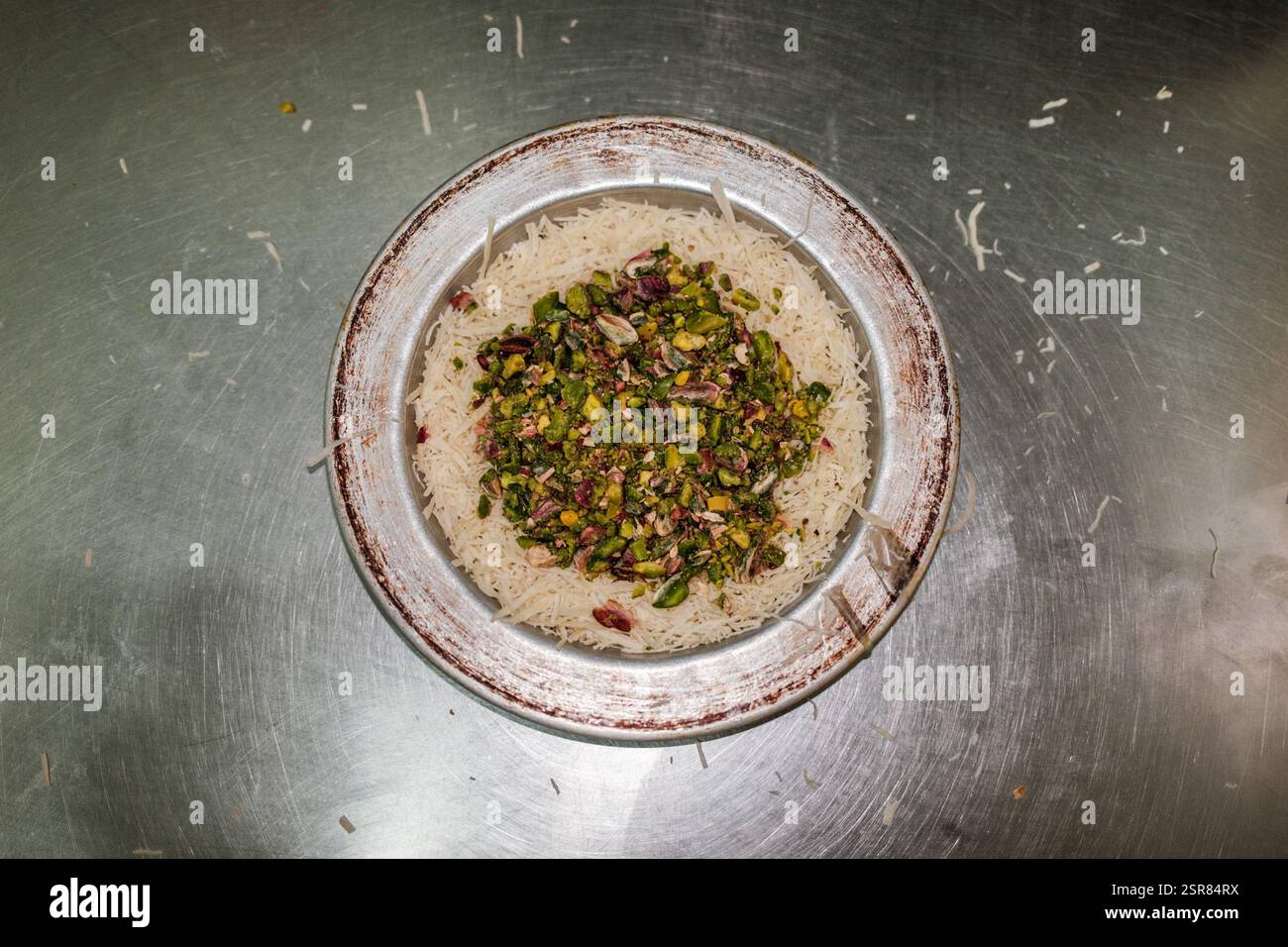 Hatay, Antakya, Türkei. Februar 2025. Pistazien, die in die Kunafa gegossen werden. Kunafa, das berühmte Dessert des Nahen Ostens, ist der unentbehrlichste und klarste Geschmack der arabischen Küche. Das Zentrum von Kunafa ist Antakya, eine ehemalige syrische Provinz. Von der osmanischen Zeit bis heute hat Antakya Kunafa seinen Ruf berühmt gemacht. Antakya Kunafa ist eines der wenigen in der Türkei hergestellten Desserts mit Käse. In der Herstellung von Kadayif werden frischer Kunafa-Käse, Butter und Sherbet verwendet. Er wird durch Kochen von Kunafa-Käse zwischen zwei Lagen Drahtsadayif gewonnen Stockfoto