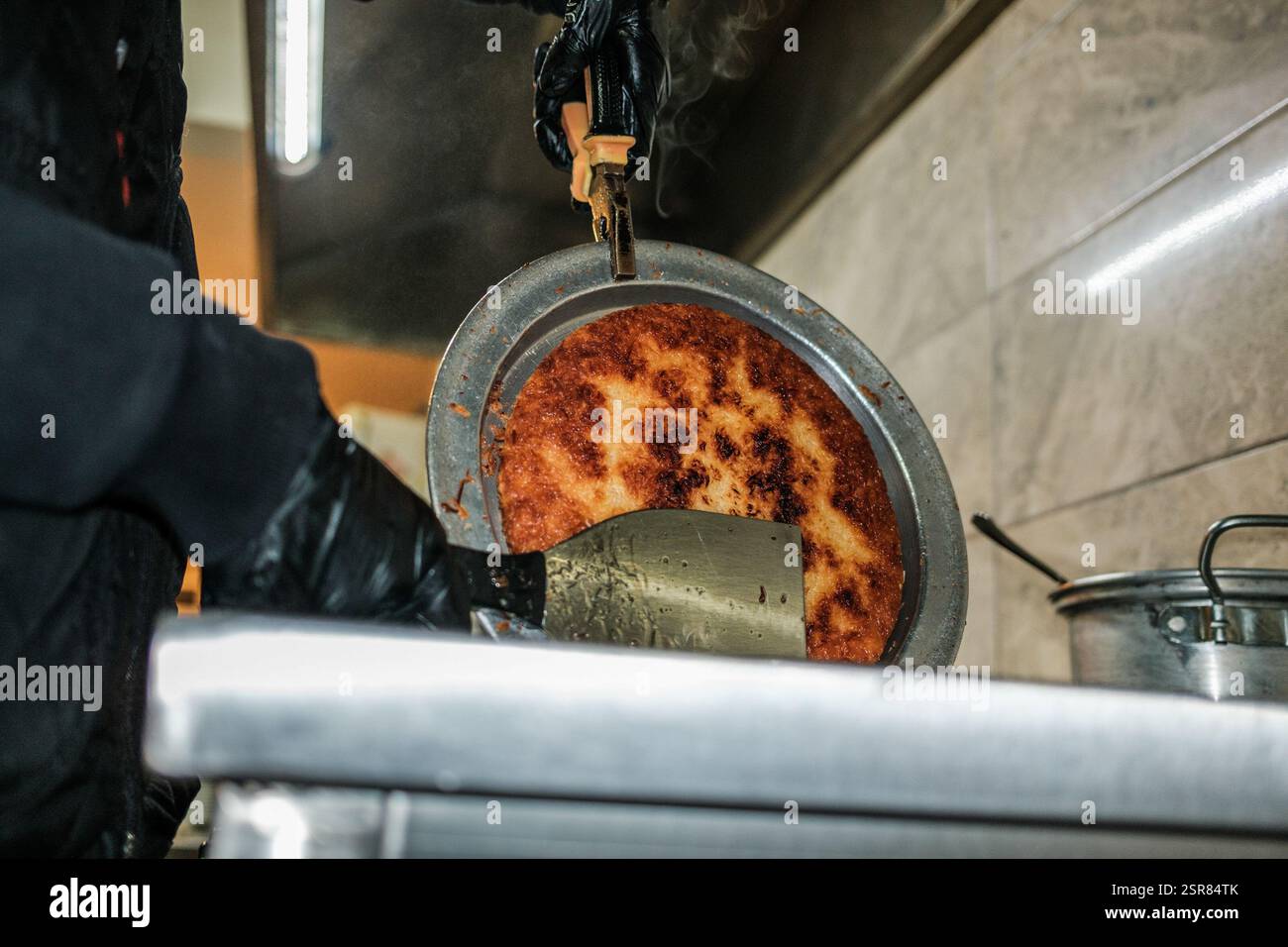 Hatay, Antakya, Türkei. Februar 2025. Das überschüssige Öl tritt nach dem Kochen aus der Kunafa aus. Kunafa, das berühmte Dessert des Nahen Ostens, ist der unentbehrlichste und klarste Geschmack der arabischen Küche. Das Zentrum von Kunafa ist Antakya, eine ehemalige syrische Provinz. Von der osmanischen Zeit bis heute hat Antakya Kunafa seinen Ruf berühmt gemacht. Antakya Kunafa ist eines der wenigen in der Türkei hergestellten Desserts mit Käse. In der Herstellung von Kadayif werden frischer Kunafa-Käse, Butter und Sherbet verwendet. Er wird durch das Kochen von Kunafa-Käse zwischen zwei laye gewonnen Stockfoto