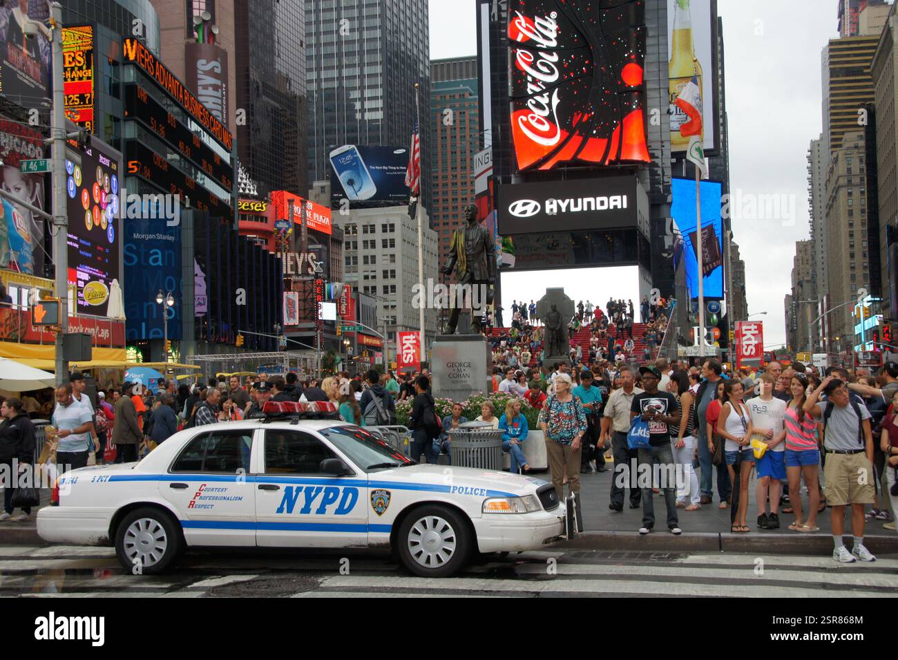 Manhattans Wächter teilen ein Geheimnis. Ein Polizeiauto mit einem Coca-Cola-Logo fährt unter dem Glühen des Times Square. Diese Szene überwindet einen Konfus Stockfoto Manhattans Wächter teilen ein Geheimnis. Ein Polizeiauto mit einem Coca-Cola-Logo fährt unter dem Glühen des Times Square. Diese Szene überwindet einen Konfus Stockfoto