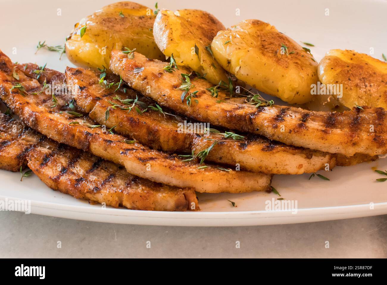 Nahaufnahme von geschnittenen gegrillten Schweinekoteletts mit knusprigen Kartoffeln und frischer Thymian-Garnele Stockfoto