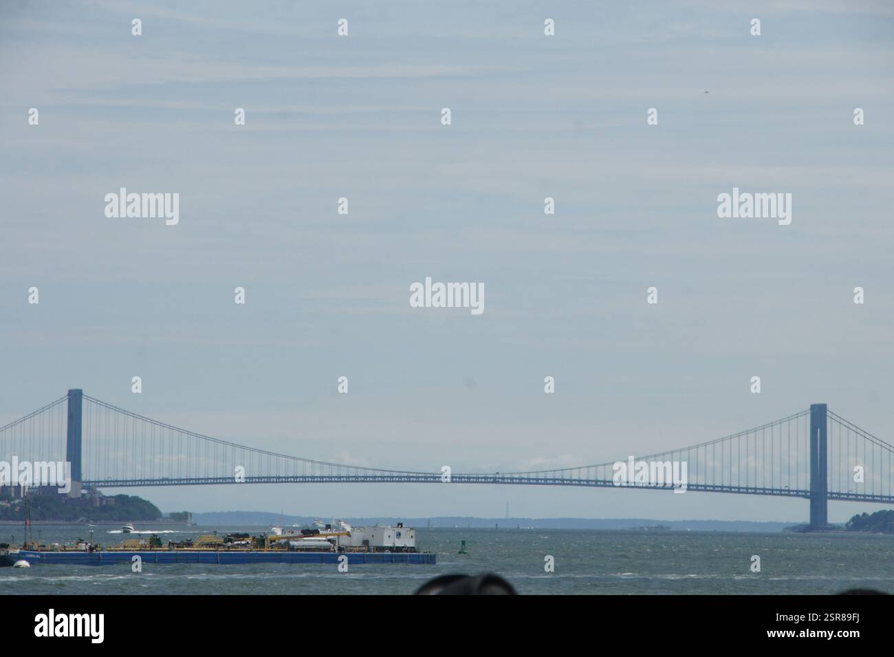 Eine malerische Szene des New Yorker Hafens entfaltet sich, mit einem einsamen Boot, das ruhig im Wasser wippt, das von der majestätischen Verrazzano-Narrows Bridge-Straße gedämpft wird Stockfoto