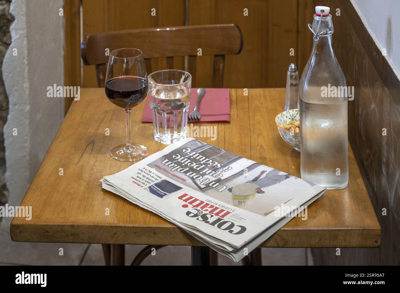Taverentisch mit Corse Matin Zeitung, Rotweinglas, Wasserflasche mit Glas, Besteck, Salz und Pfeffer im U PaeseVivario Country inn, PNR Corse, C Stockfoto