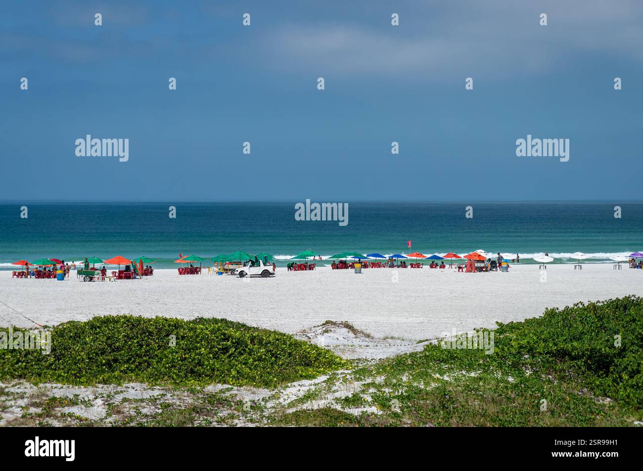 Teilweiser Blick auf den Strand Praia Grande mit leuchtenden Sonnenschirmen und klarem Atlantikwasser unter hellem Sommermorgen, heißem, sonnigem, klarem blauem Himmel. Stockfoto
