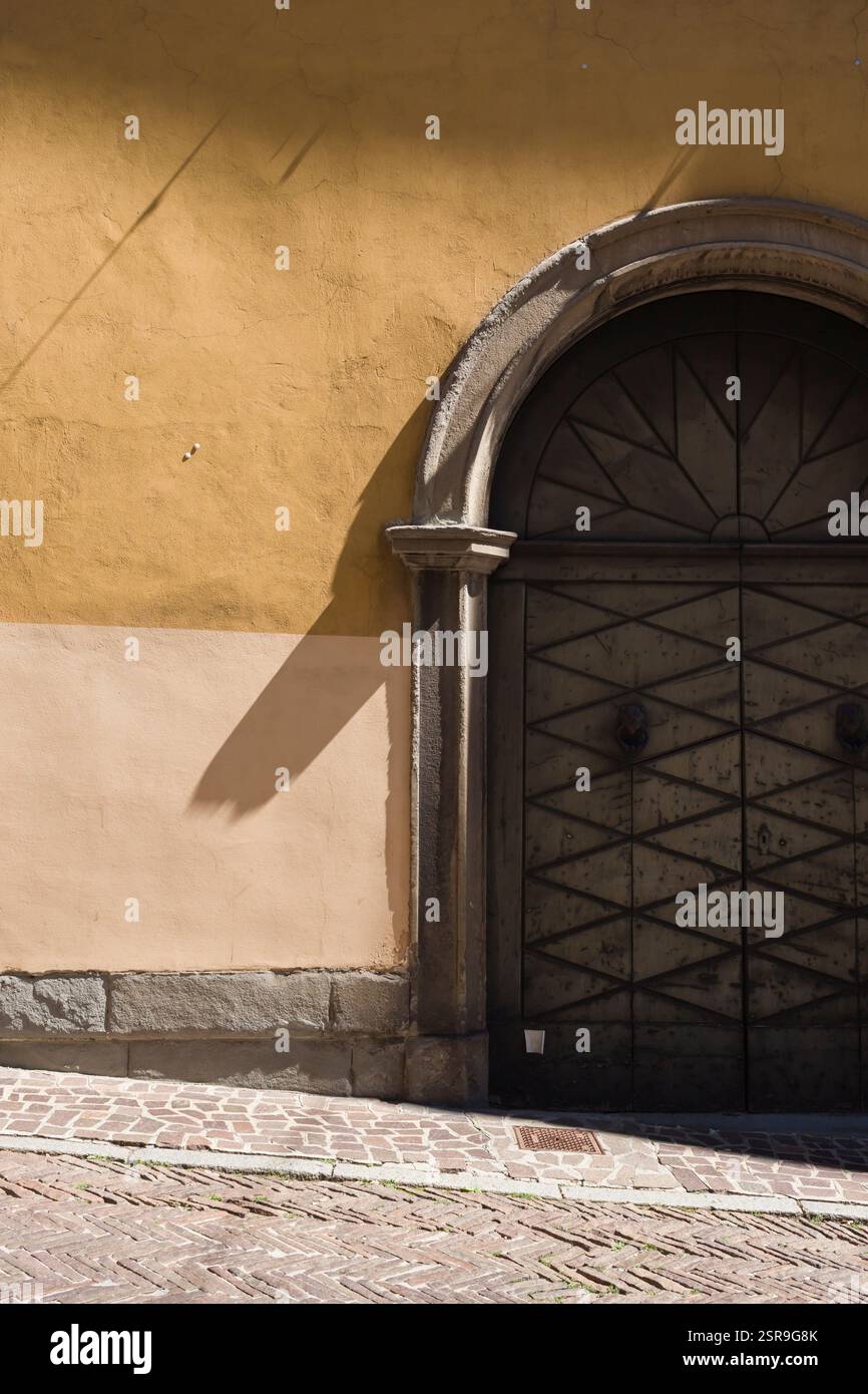 Eine alte Holztür im Torbogen einer gelben Mauer in einer Kopfsteinpflasterstraße in Bergamo, Citta Bassa historisches Zentrum. Stockfoto