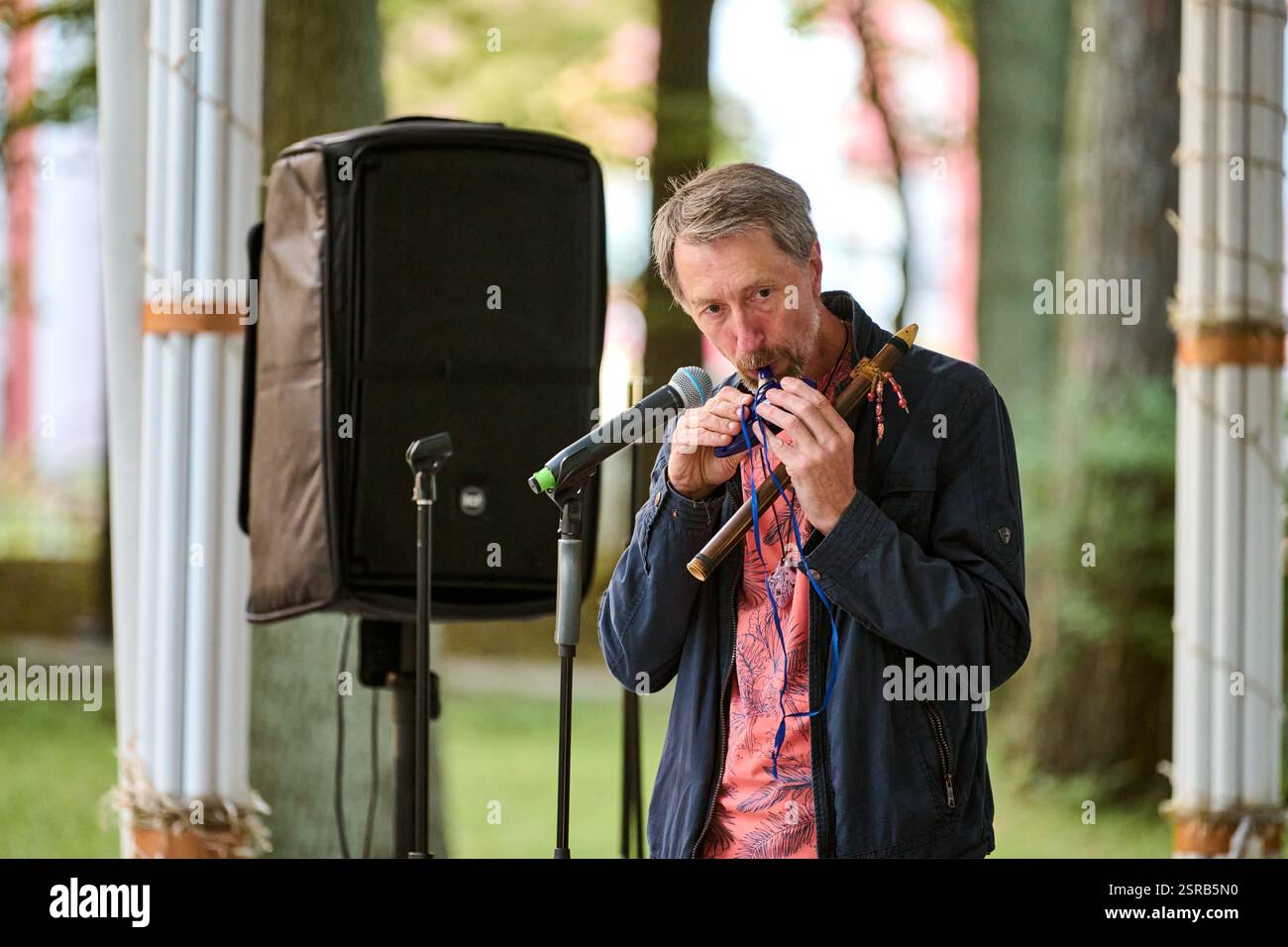 Kaliningrad, Russland - 10.08.2024 - Reifer Mann spielt im Freien Blasinstrument, in Musik vertieft. Sanfte Beleuchtung, grüner Hintergrund sorgt für eine ruhige Atmosphäre Stockfoto